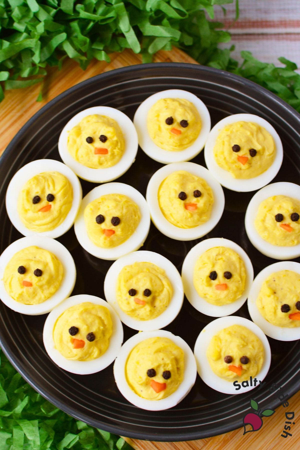 overhead view of chick deviled eggs on a black platter decorated with peppercorn eyes and carrot beaks