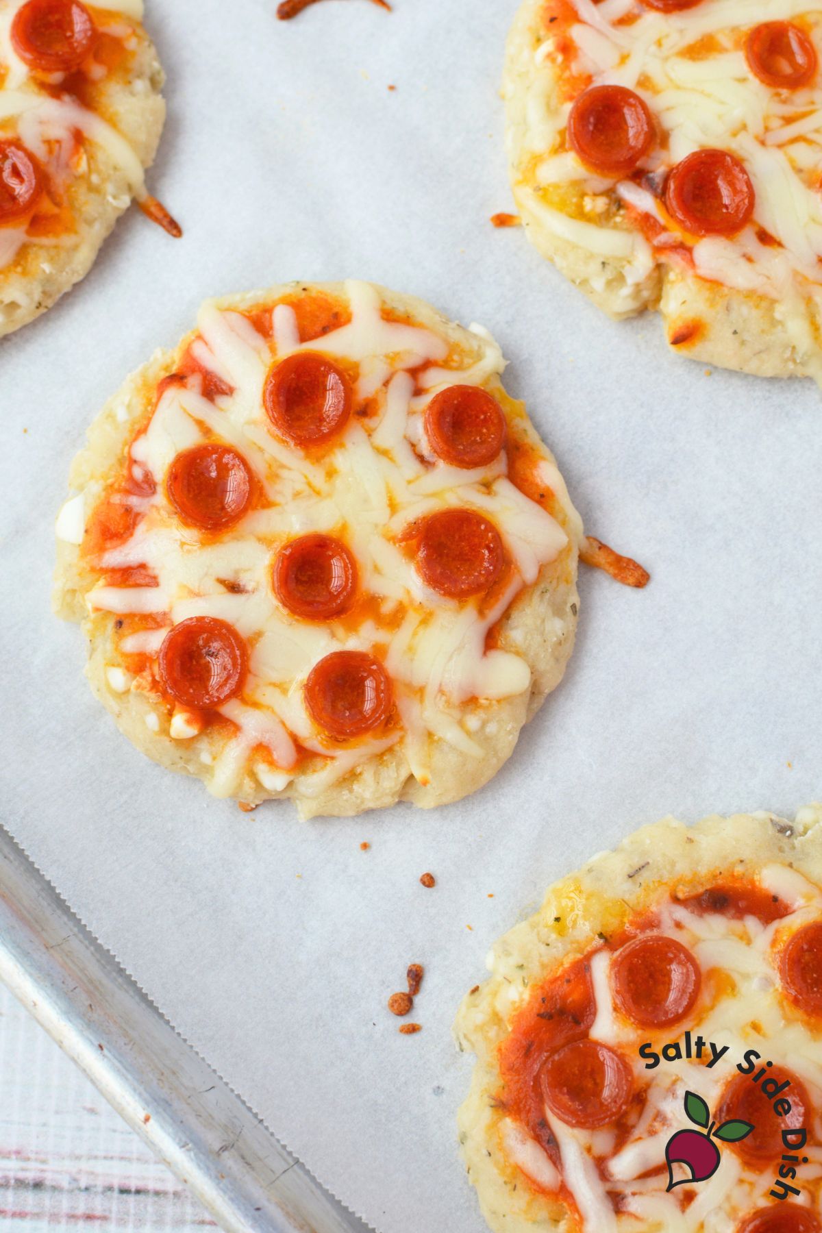 close up of baked cottage cheese mini pizza on parchment paper topped with melted mozzarella and mini pepperoni