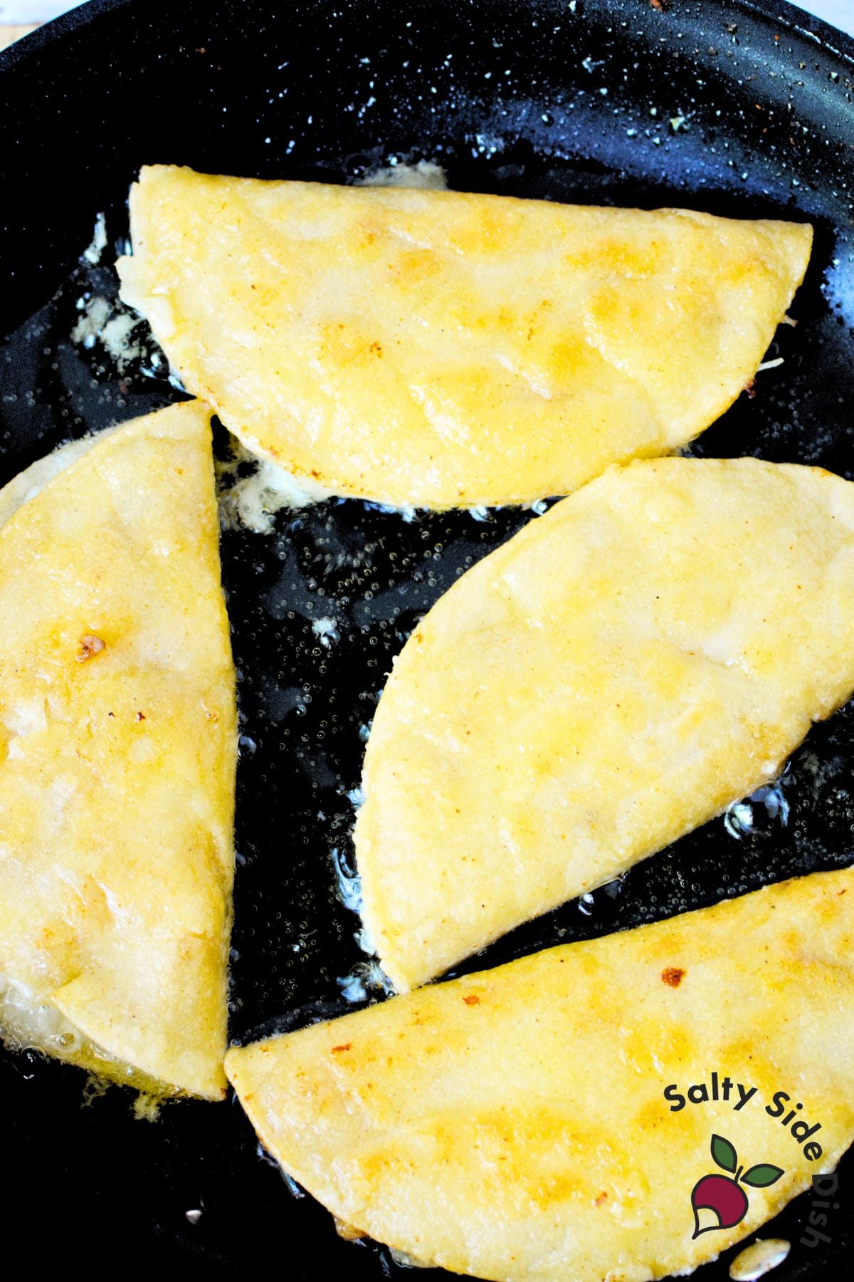 Three folded chicken tacos frying in vegetable oil in black skillet until golden and crispy