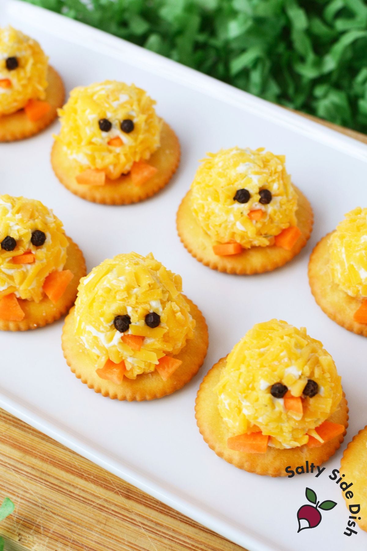 mini chick cheeseball bites on a white serving tray decorated with peppercorn eyes and carrot beaks surrounded by green Easter grass