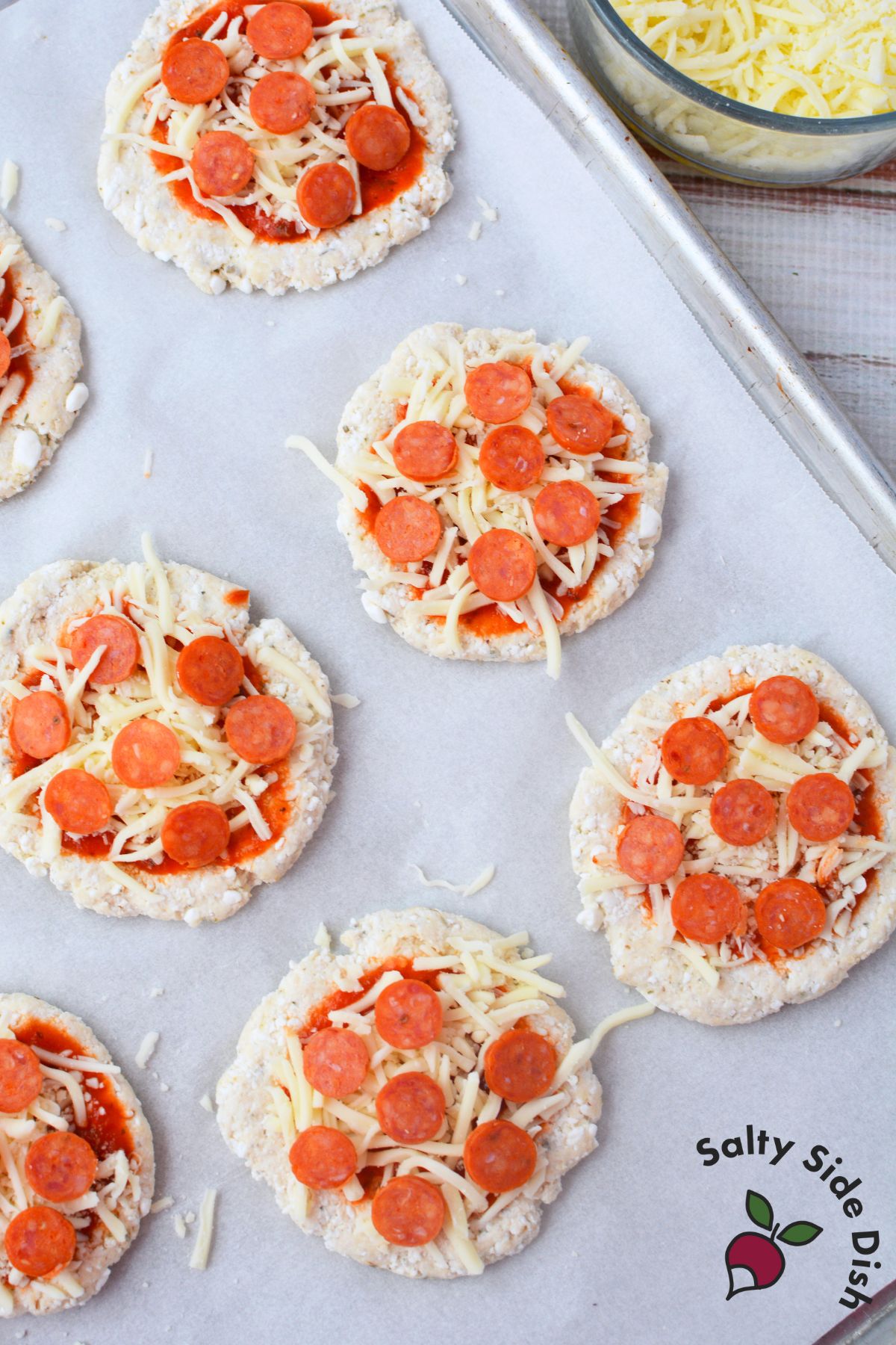 cottage cheese pizza rounds on baking sheet topped with pizza sauce, shredded mozzarella, and mini pepperoni before baking