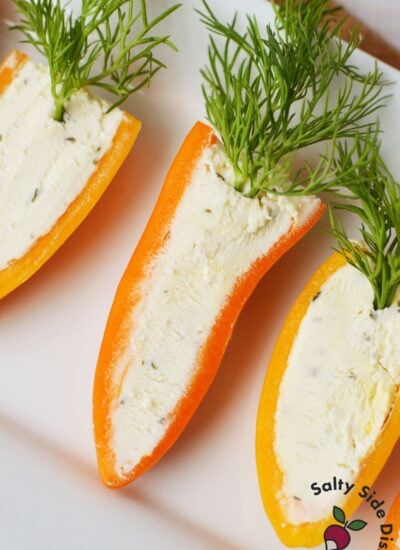 Close up of three stuffed mini pepper carrots filled with Boursin cheese and topped with fresh dill on a white platter