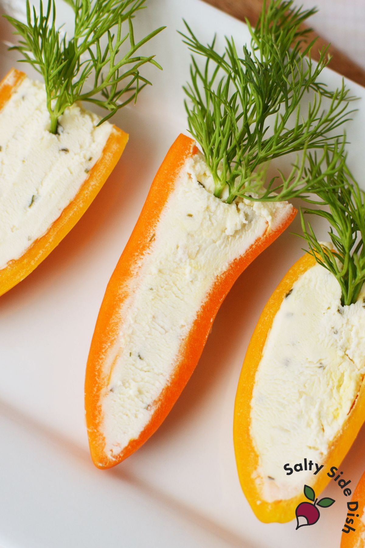 Close up of three stuffed mini pepper carrots filled with Boursin cheese and topped with fresh dill on a white platter