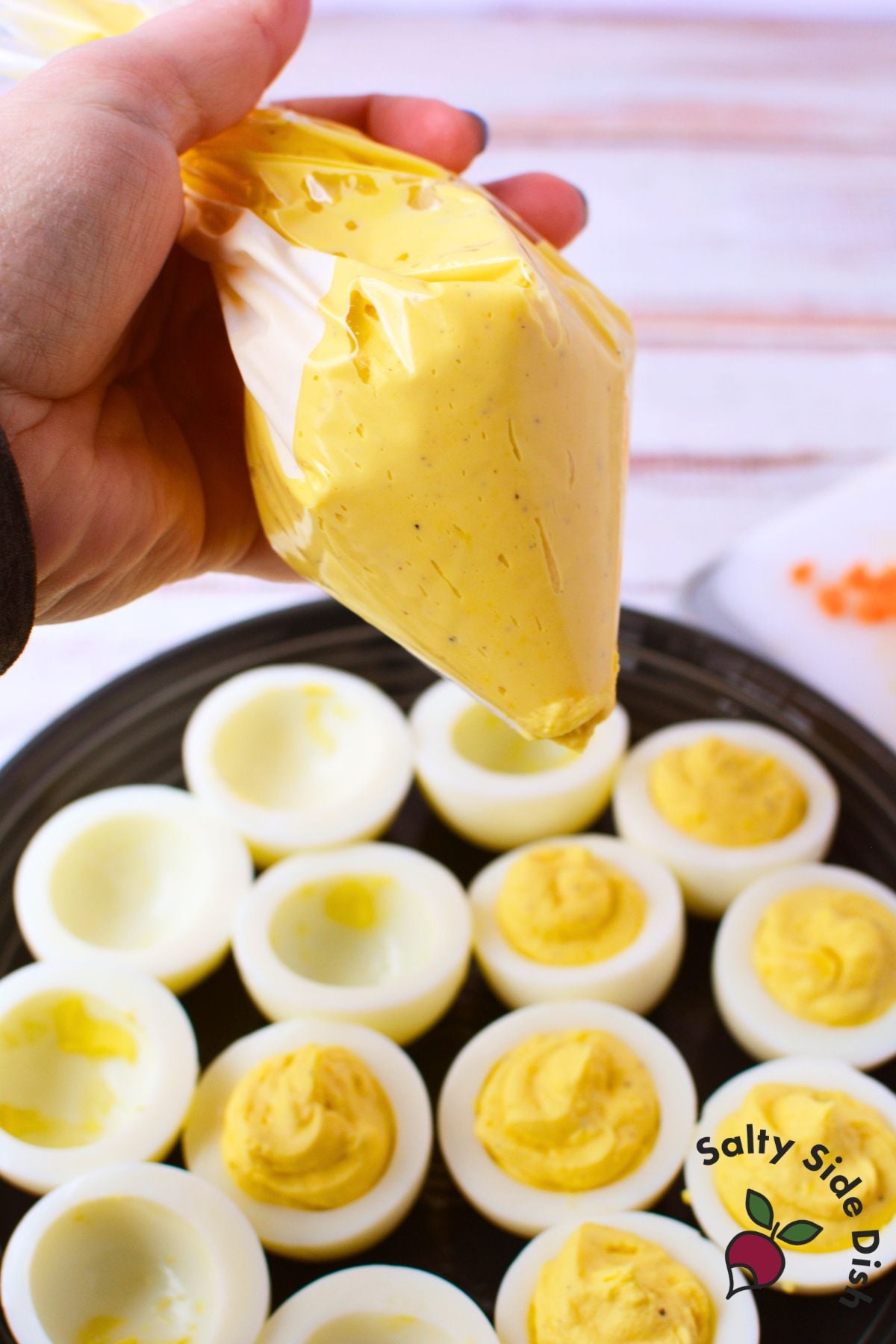 piping creamy deviled egg filling into crosswise cut egg halves on a black platter