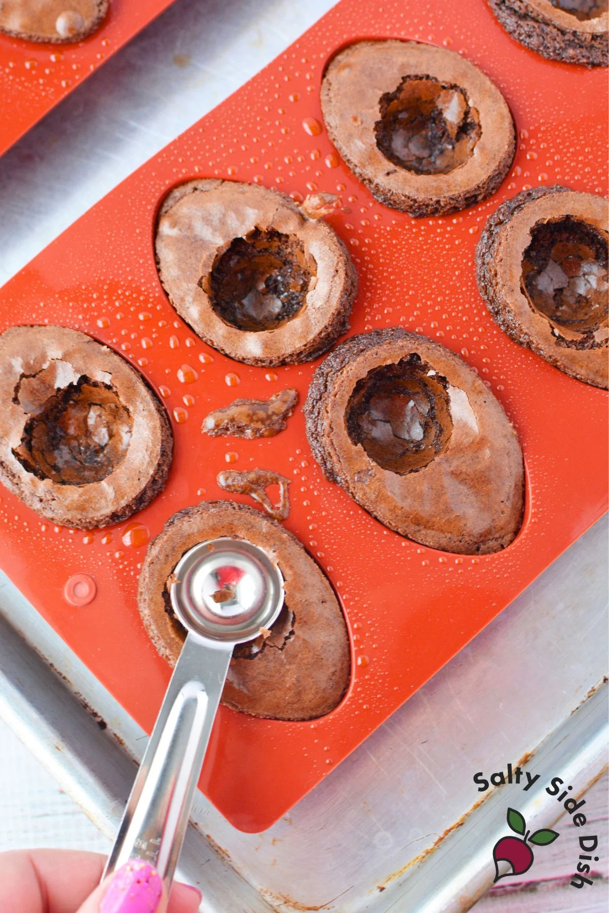 Removing baked brownie eggs from silicone molds using a spoon to create hollow centers