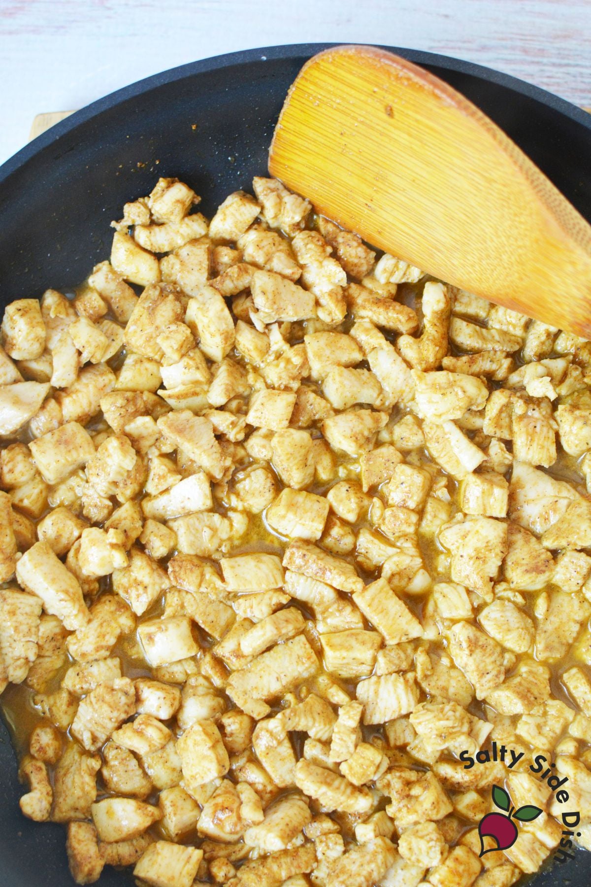 Diced chicken breast cooking with taco seasoning in a black skillet with wooden spoon