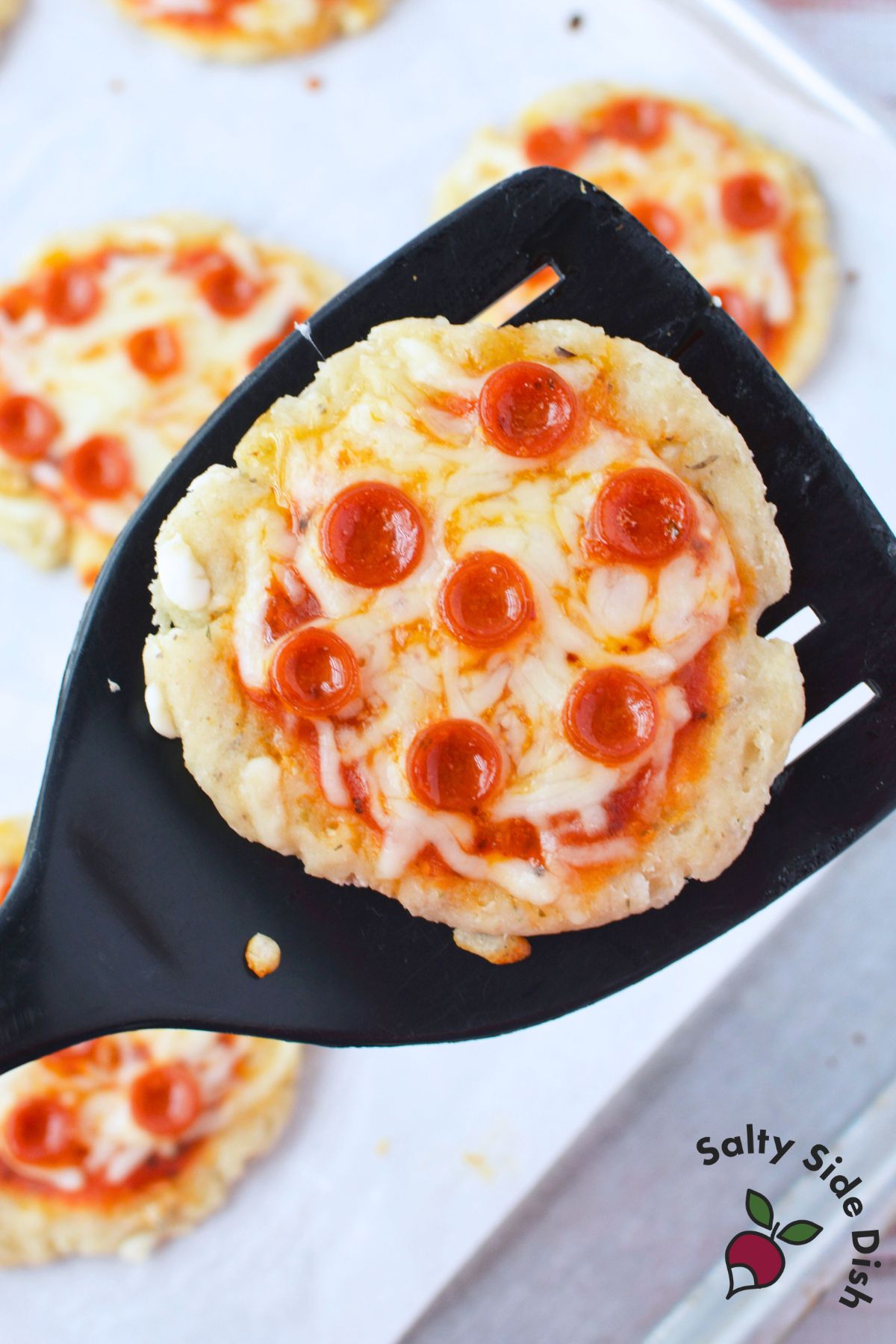 baked cottage cheese mini pepperoni pizza lifted on a black spatula fresh from the oven
