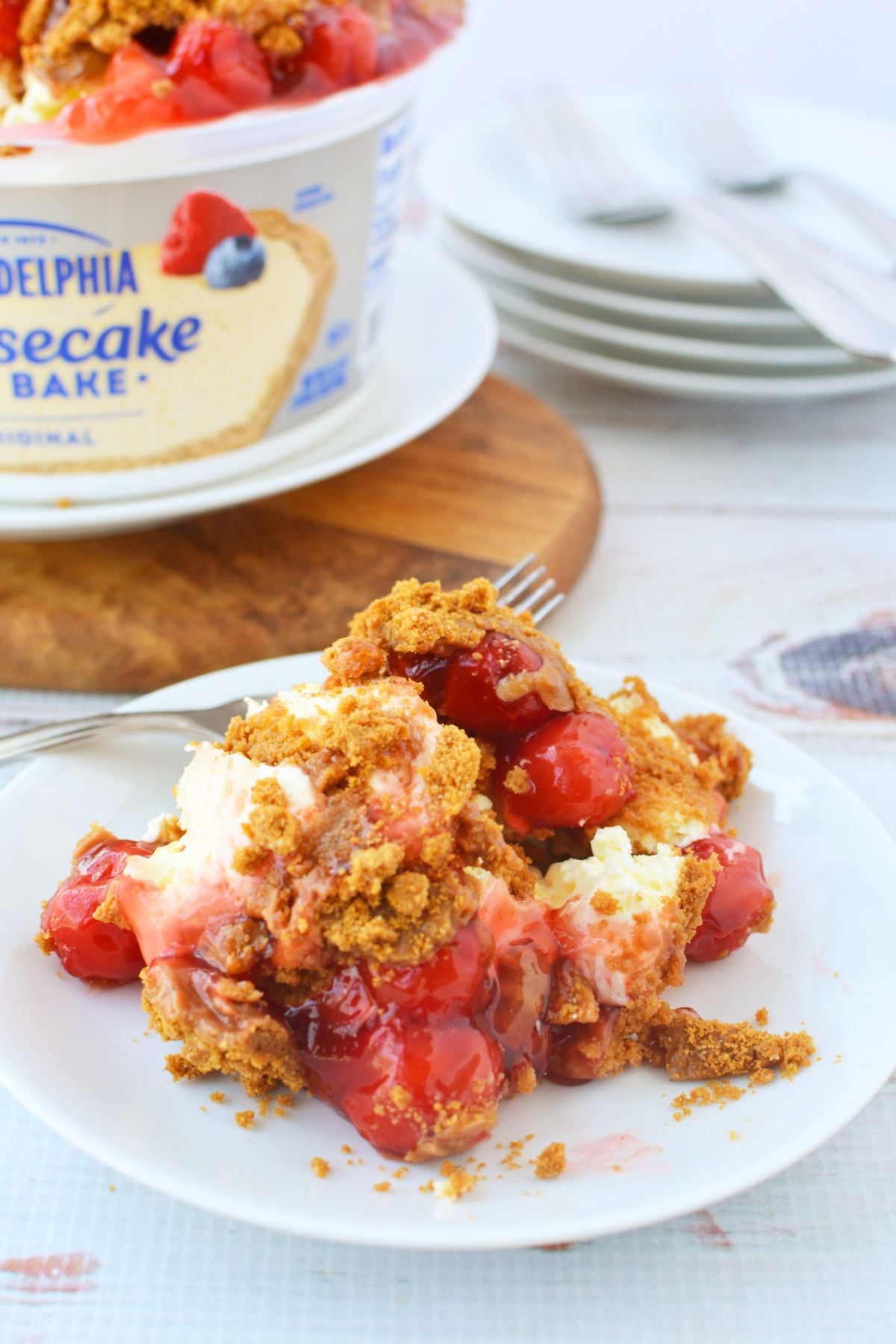 Served slice of no bake cheesecake with cherry topping and crushed Biscoff cookies on white plate
