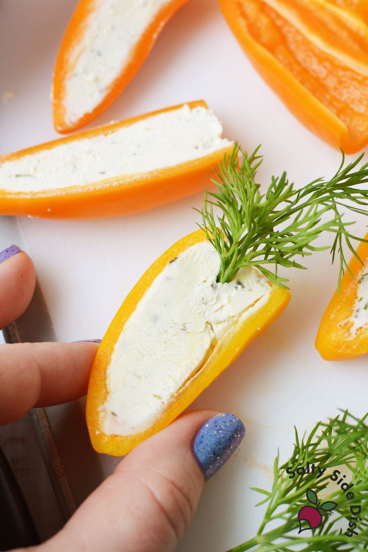 Hand pressing fresh dill into a Boursin stuffed mini pepper half to look like a carrot top