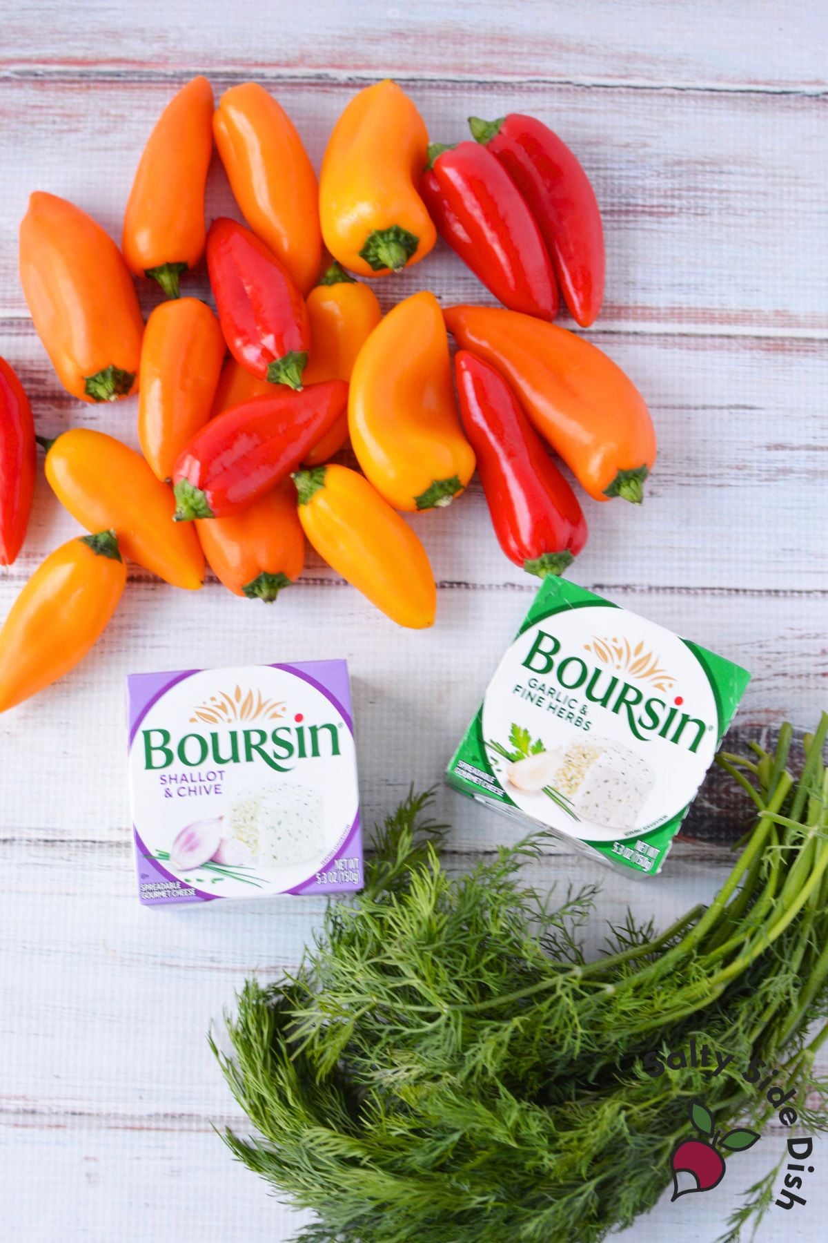 Mini bell peppers, Boursin shallot chive, Boursin garlic and fine herbs, and fresh dill arranged on a white wood surface