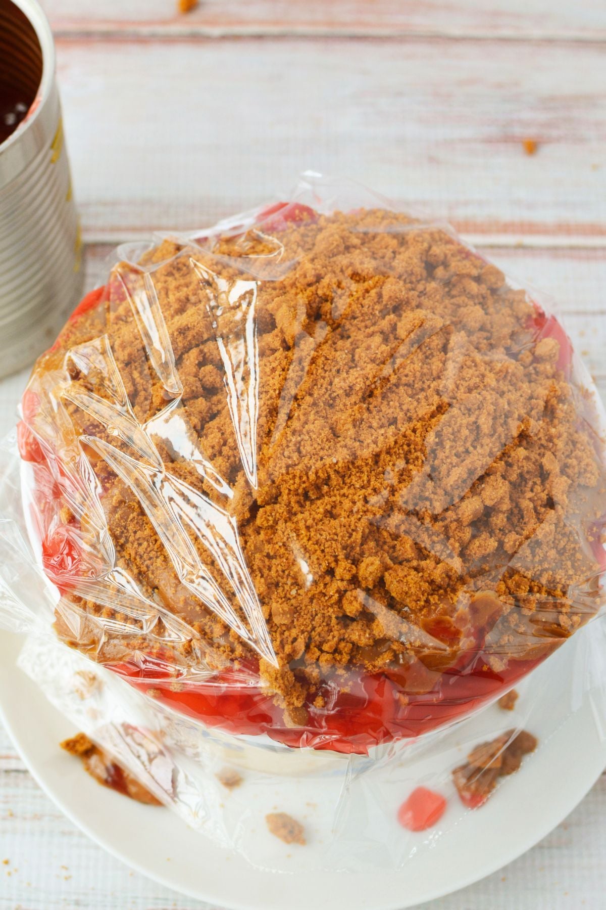 No bake cherry Biscoff cheesecake wrapped in plastic wrap for refrigerator storage