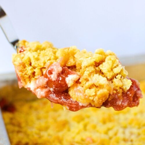 close up spoonful of cherry cheesecake dump cake with golden crumble topping and glossy cherry filling lifted from baking pan