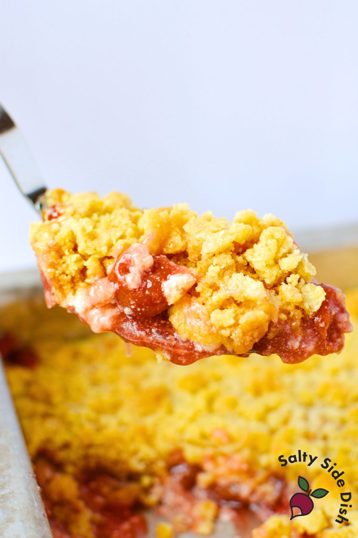 close up spoonful of cherry cheesecake dump cake with golden crumble topping and glossy cherry filling lifted from baking pan