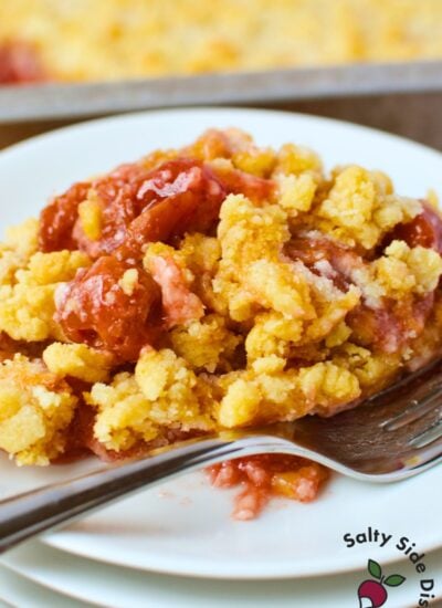 plated serving of cherry cheesecake dump cake with buttery golden crumble and cherry filling, fork resting on white plate