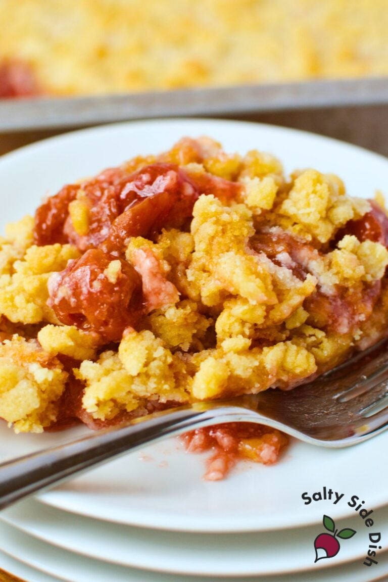 plated serving of cherry cheesecake dump cake with buttery golden crumble and cherry filling, fork resting on white plate