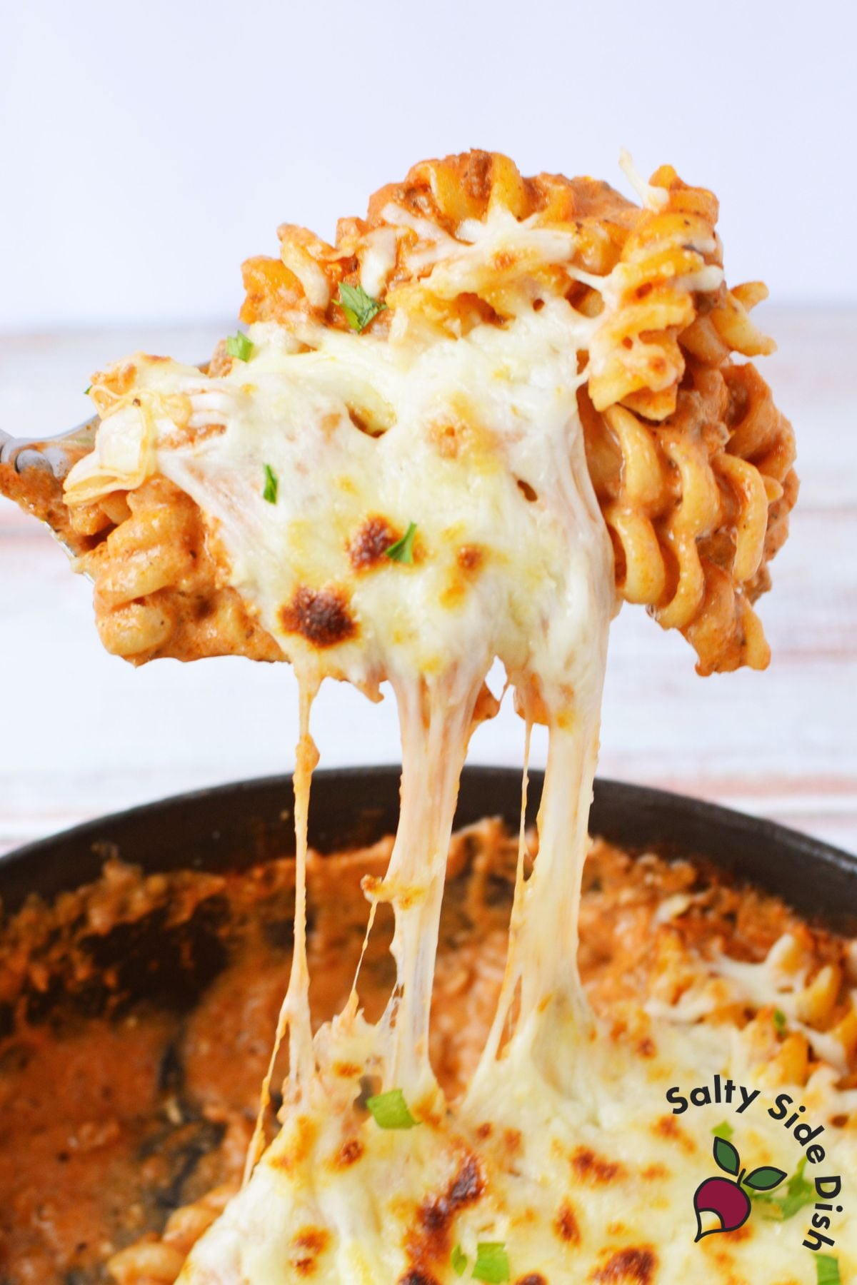 easy cheesy pasta with ground beef recipe in a cast iron skillet with broiled mozzarella and fresh parsley