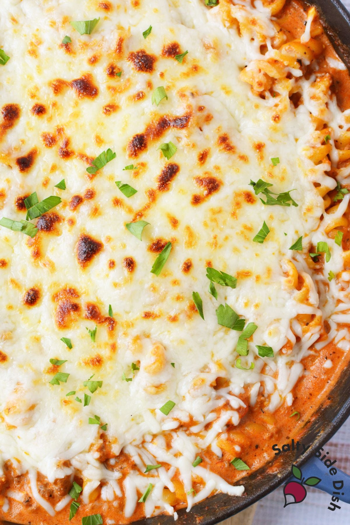 easy cheesy pasta with ground beef close up showing bubbly broiled mozzarella cheese topping with parsley