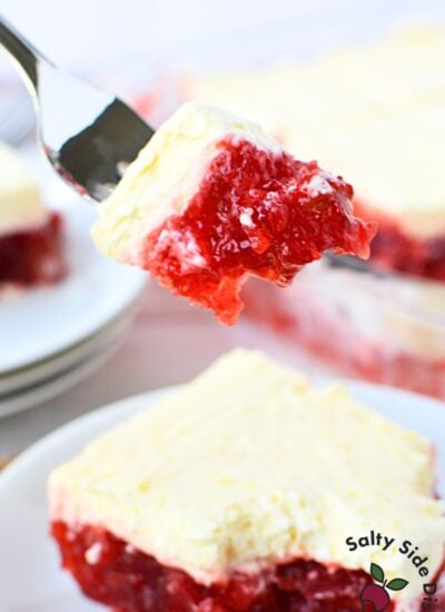 Fork holding a bite of cherry jello salad with vanilla pudding topping, showing the bright red jello layer inside