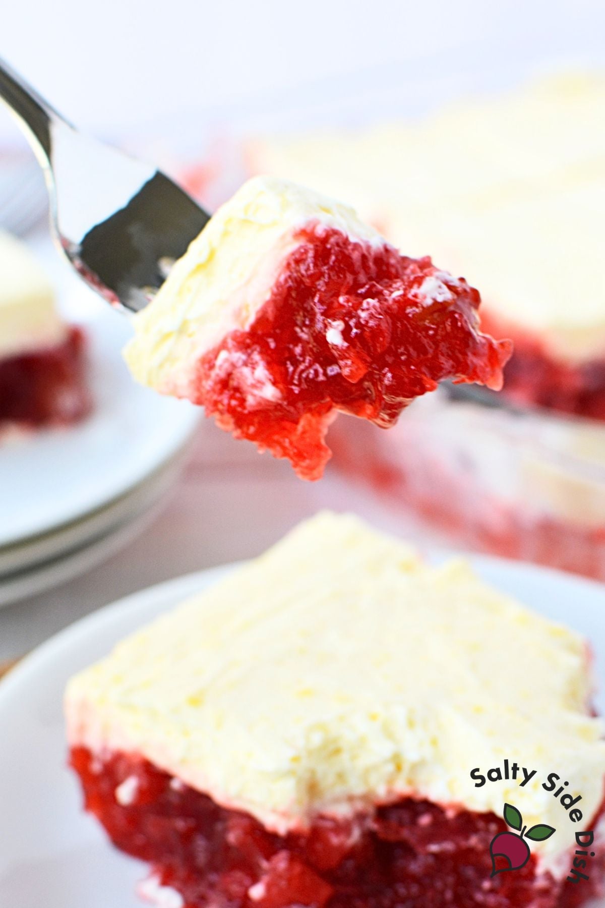 Fork holding a bite of cherry jello salad with vanilla pudding topping, showing the bright red jello layer inside