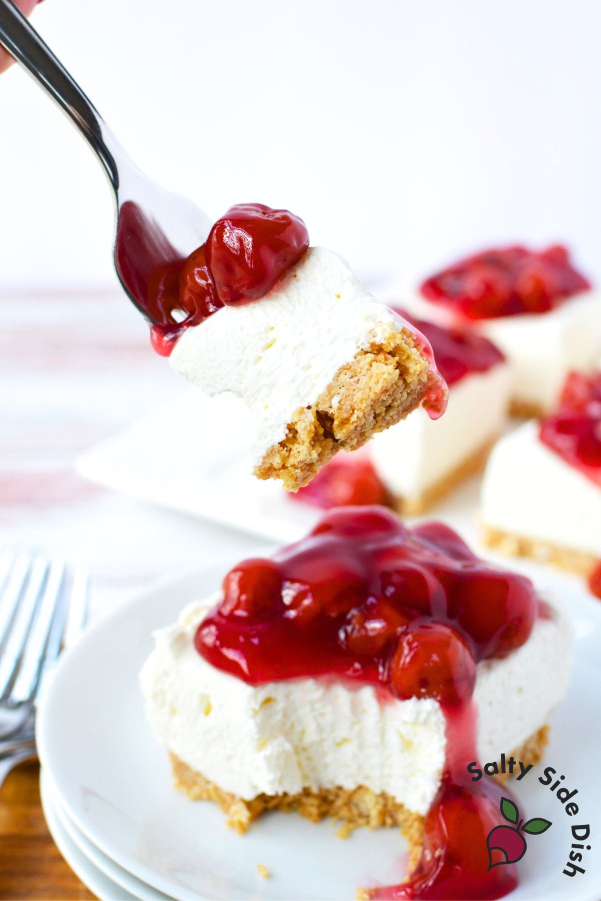 fork lifting a bite of no bake cherry cheesecake bar with cherry pie filling topping