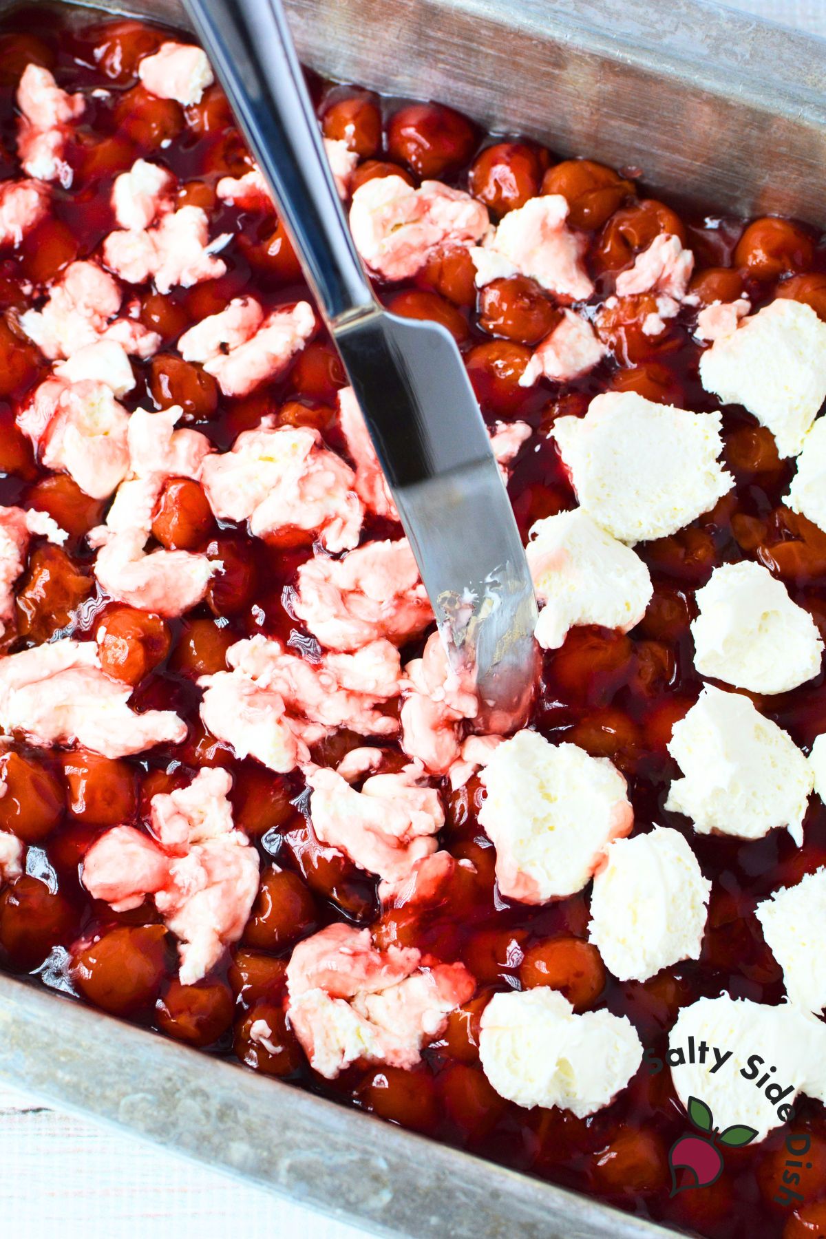 overhead view of cherry pie filling in baking pan with dollops of cream cheese being spread across the top