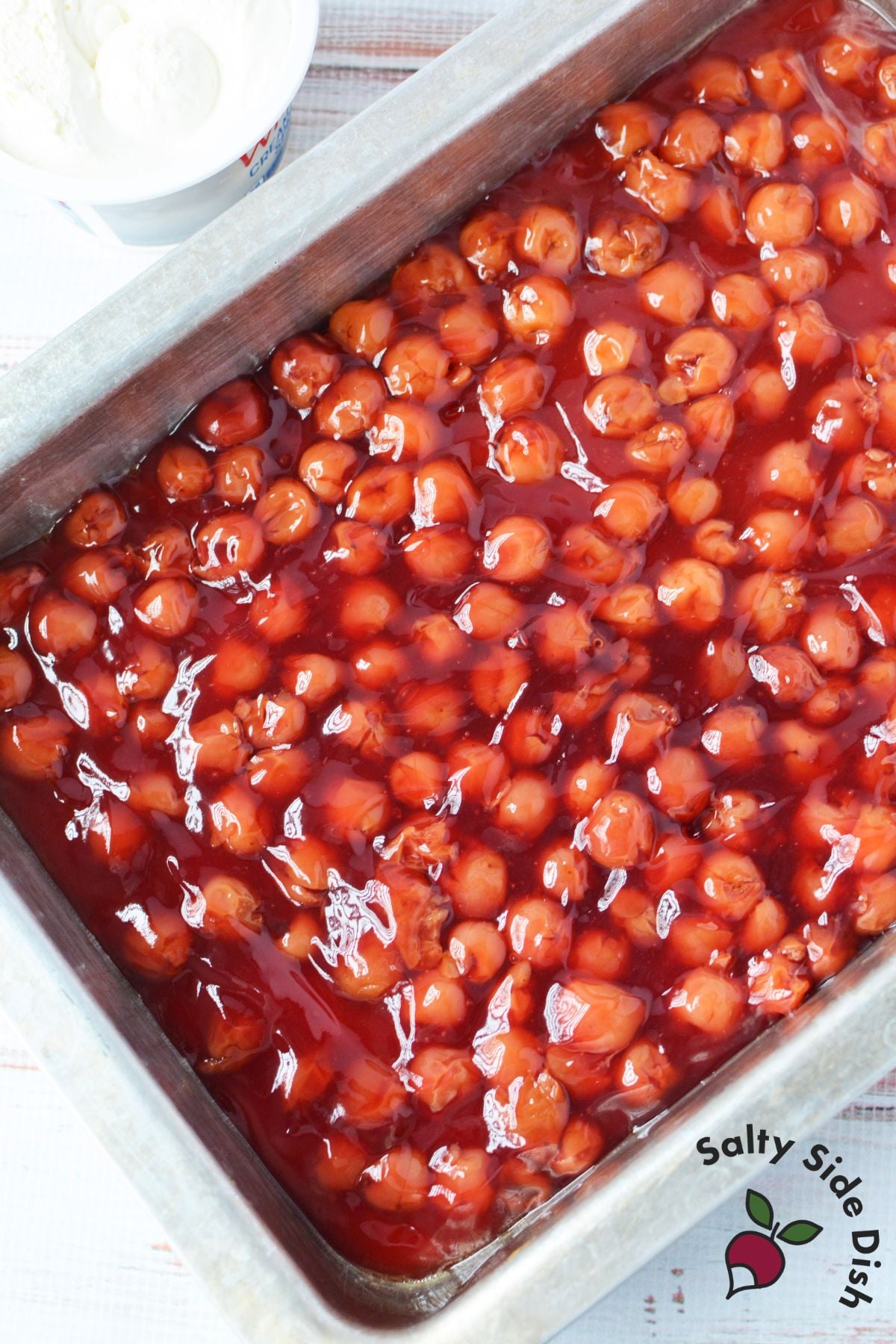 overhead view of two cans of cherry pie filling spread in a 9x13 baking pan lined with parchment