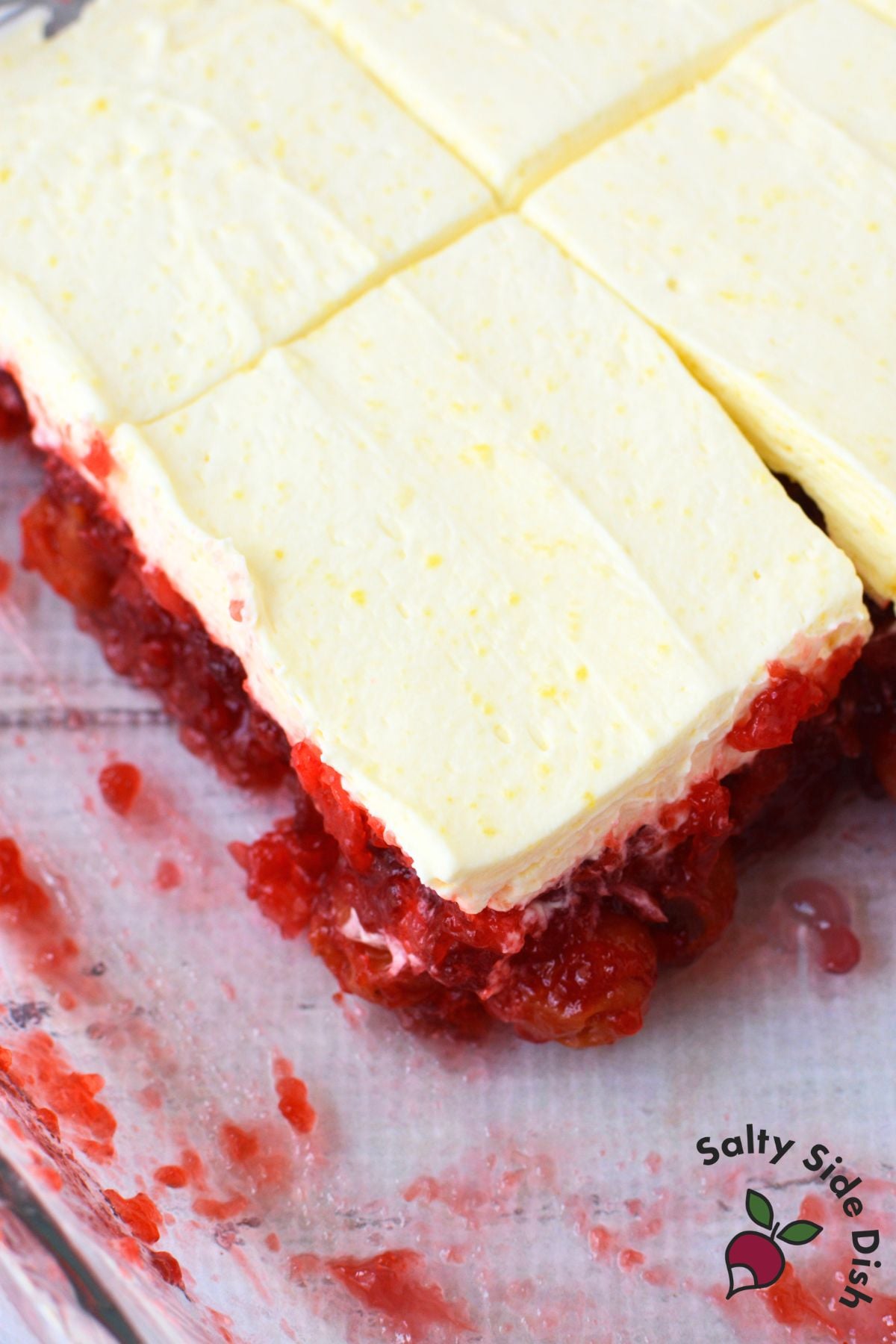 Cherry pineapple jello salad cut into squares in a glass dish, showing the bright red jello layer topped with a thick vanilla pudding whipped cream layer
