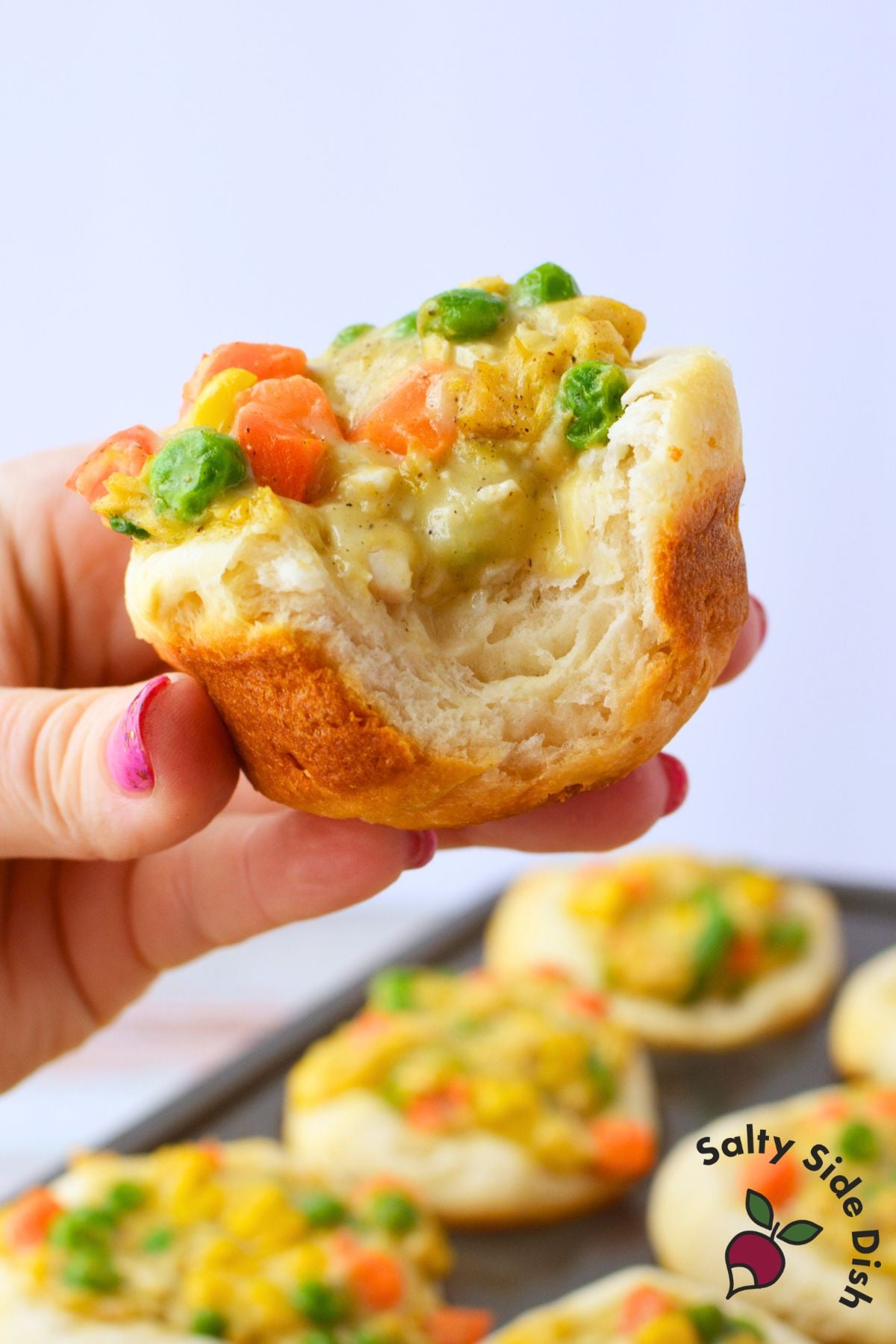 Top view of a baked chicken pot pie cup held in hand showing peas, carrots, corn, and chicken in cream of chicken sauce