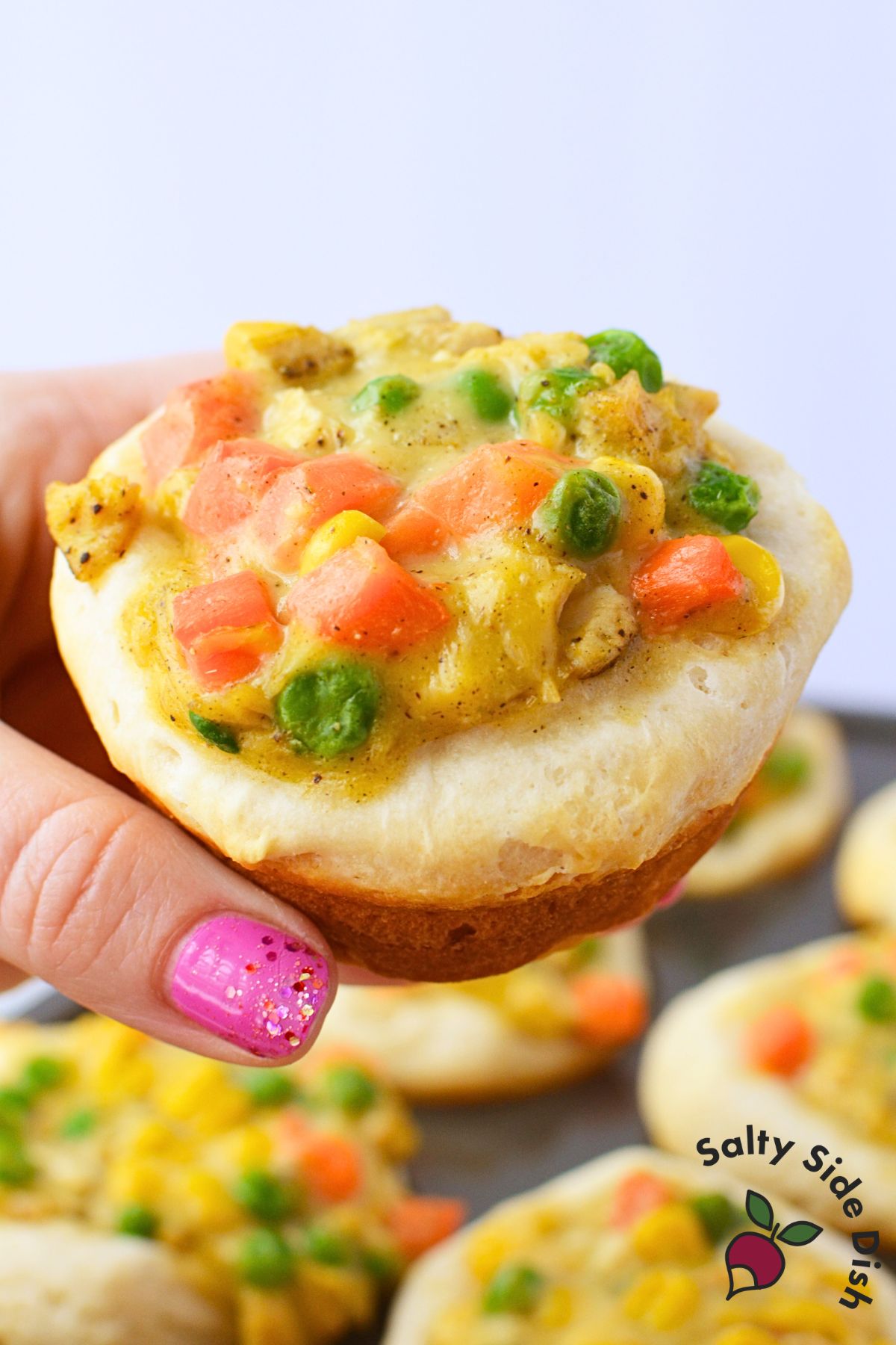 Close up of a baked chicken pot pie cup held in hand showing golden brown biscuit bottom and creamy vegetable filling