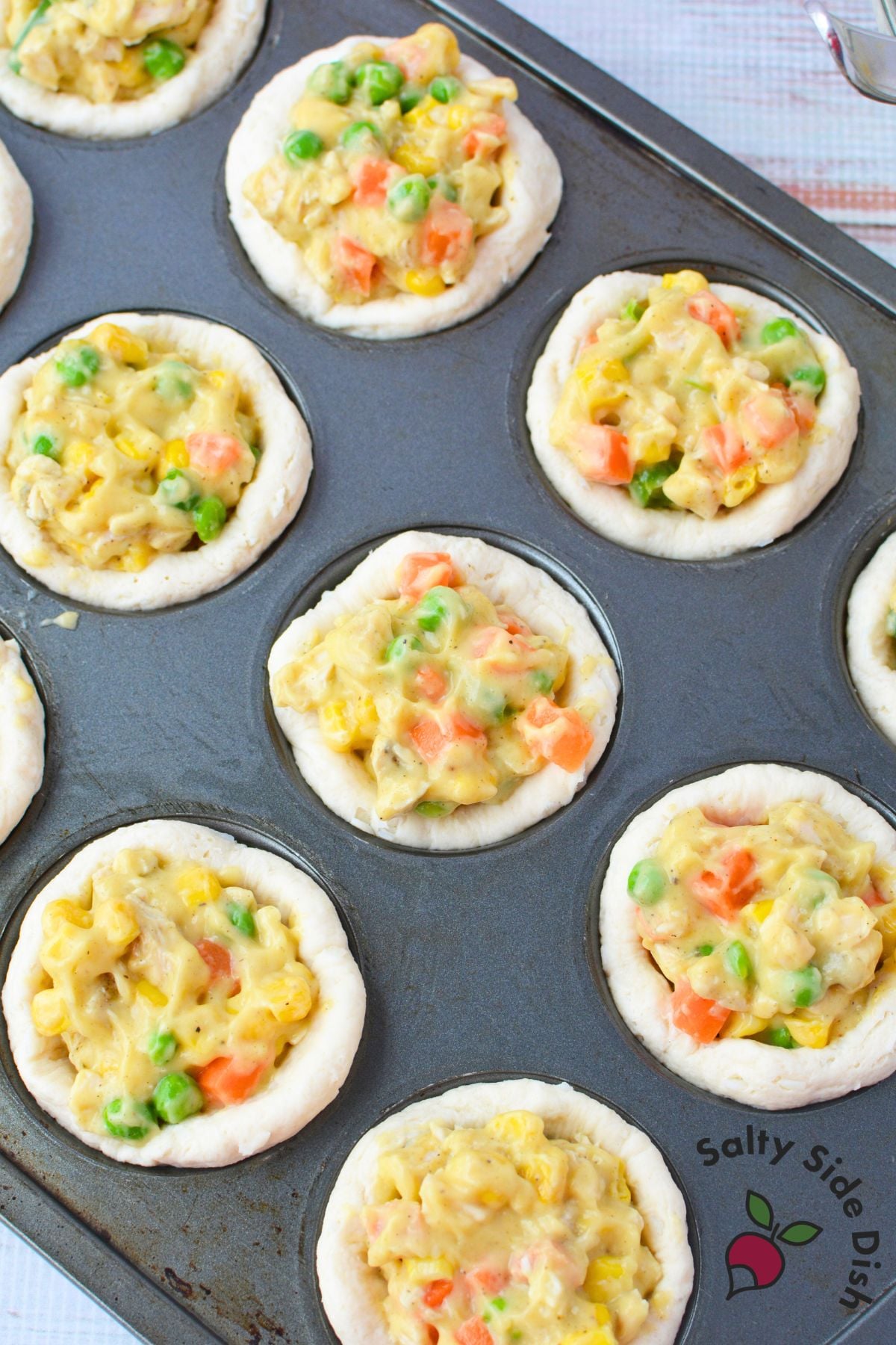 Baked chicken pot pie cups in a muffin tin with golden biscuit edges and colorful vegetable filling