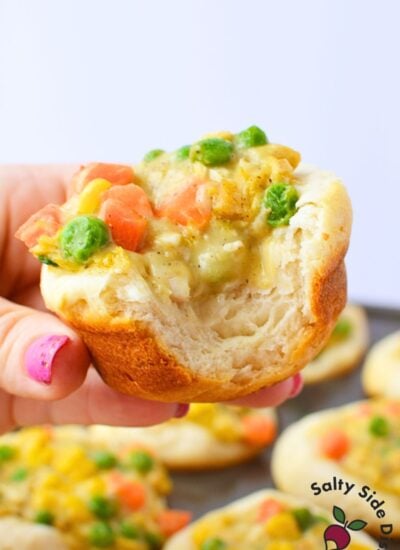 Hand holding a baked chicken pot pie cup with a bite taken showing fluffy biscuit interior and creamy chicken filling
