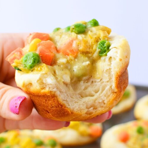Hand holding a baked chicken pot pie cup with a bite taken showing fluffy biscuit interior and creamy chicken filling