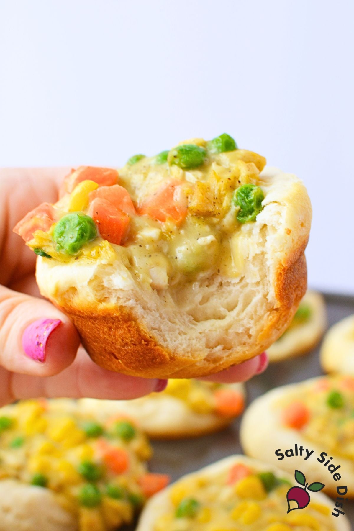 Hand holding a baked chicken pot pie cup with a bite taken showing fluffy biscuit interior and creamy chicken filling