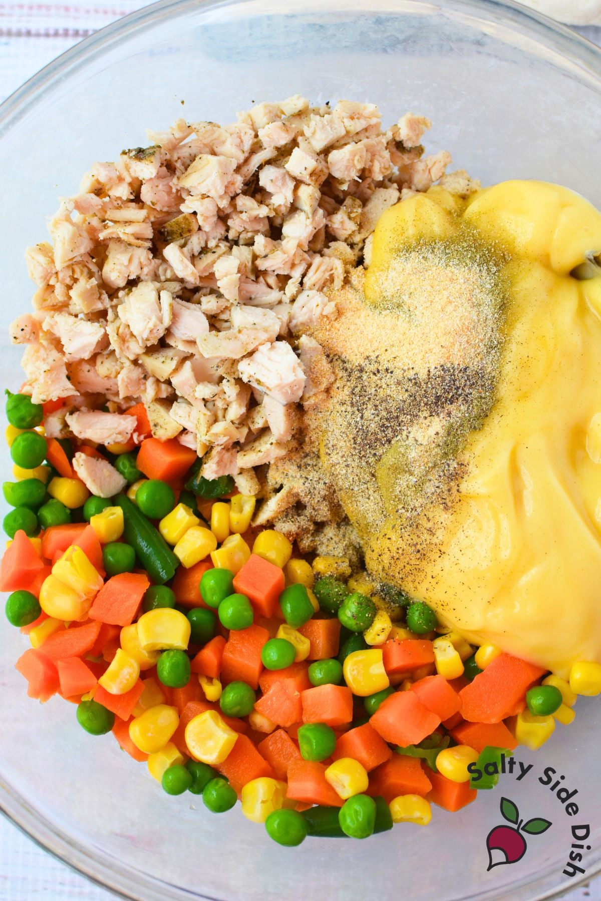 Chicken pot pie filling mixed in a glass bowl with diced chicken, cream of chicken soup, frozen peas, carrots, and corn