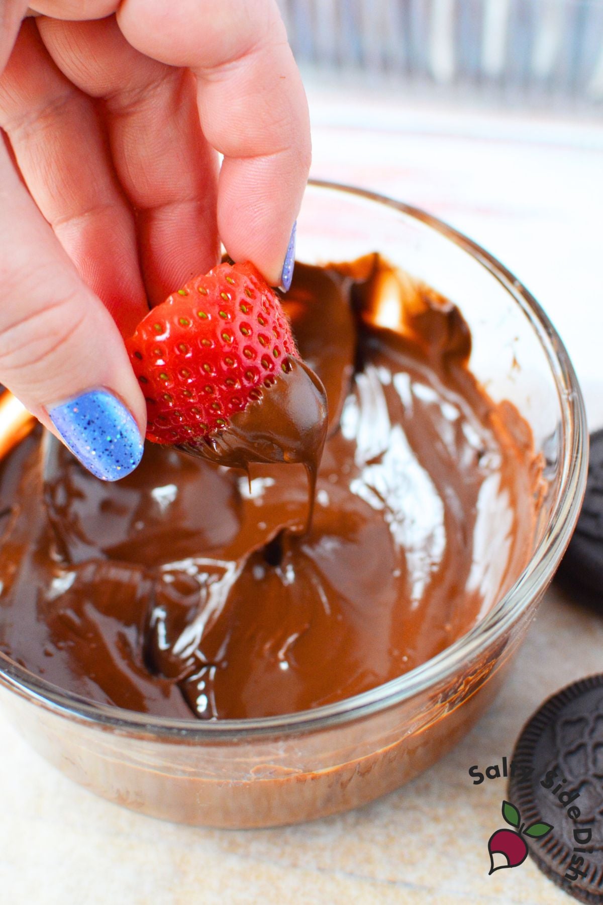 Dipping a fresh strawberry half into a bowl of melted chocolate to make strawberry ladybugs