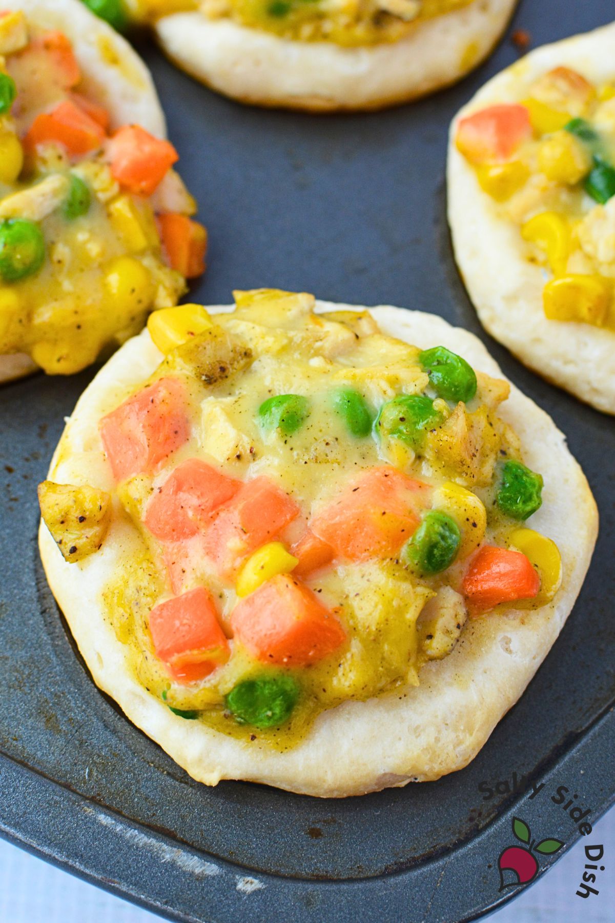 Muffin tin filled with unbaked chicken pot pie cups showing creamy filling with peas, carrots, and corn