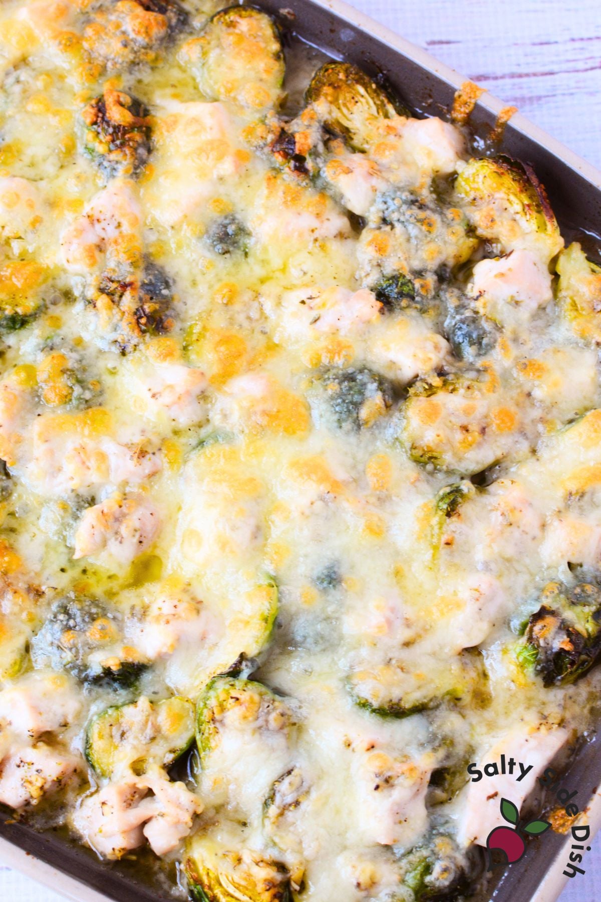 cheesy chicken and brussels sprouts being lifted from the sheet pan showing a dramatic gruyere cheese pull
