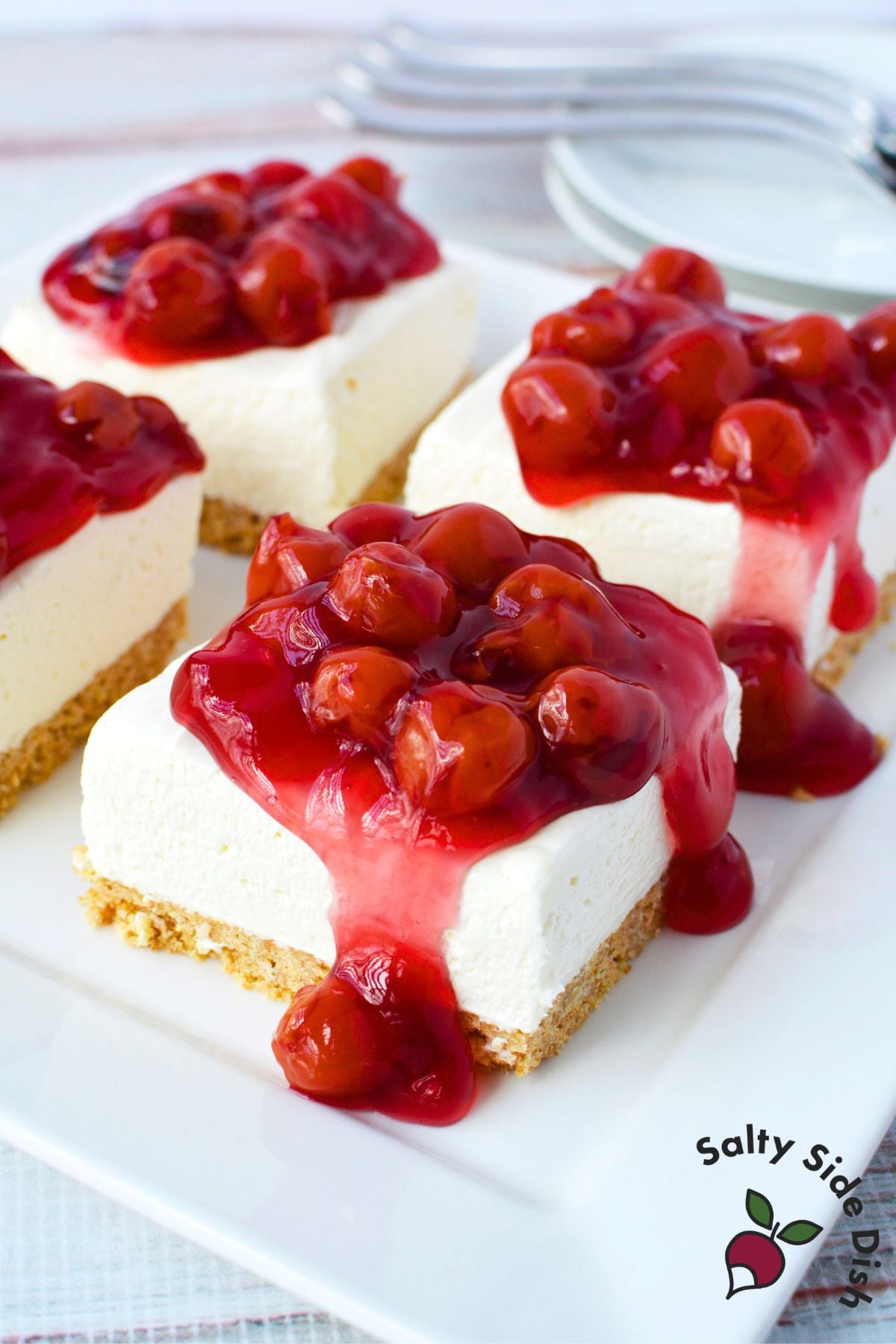 three no bake cherry cheesecake bars with cool whip filling on a white serving platter topped with cherry pie filling