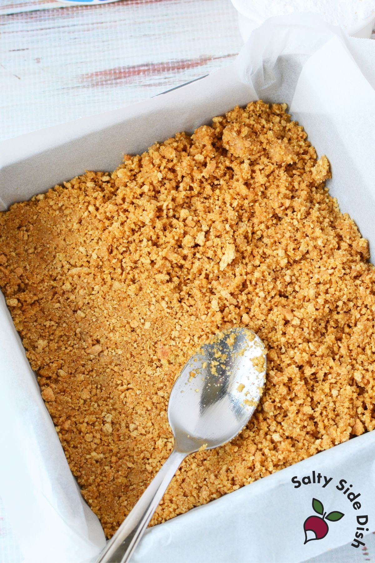 homemade graham cracker crust pressed into parchment lined 8x8 pan for no bake cheesecake bars