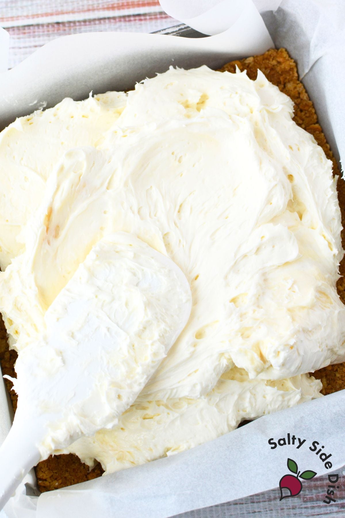 fluffy cool whip cream cheese filling spread over graham cracker crust in parchment lined pan