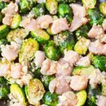 raw chicken and brussels sprouts seasoned with garlic butter spread out on a sheet pan ready to bake