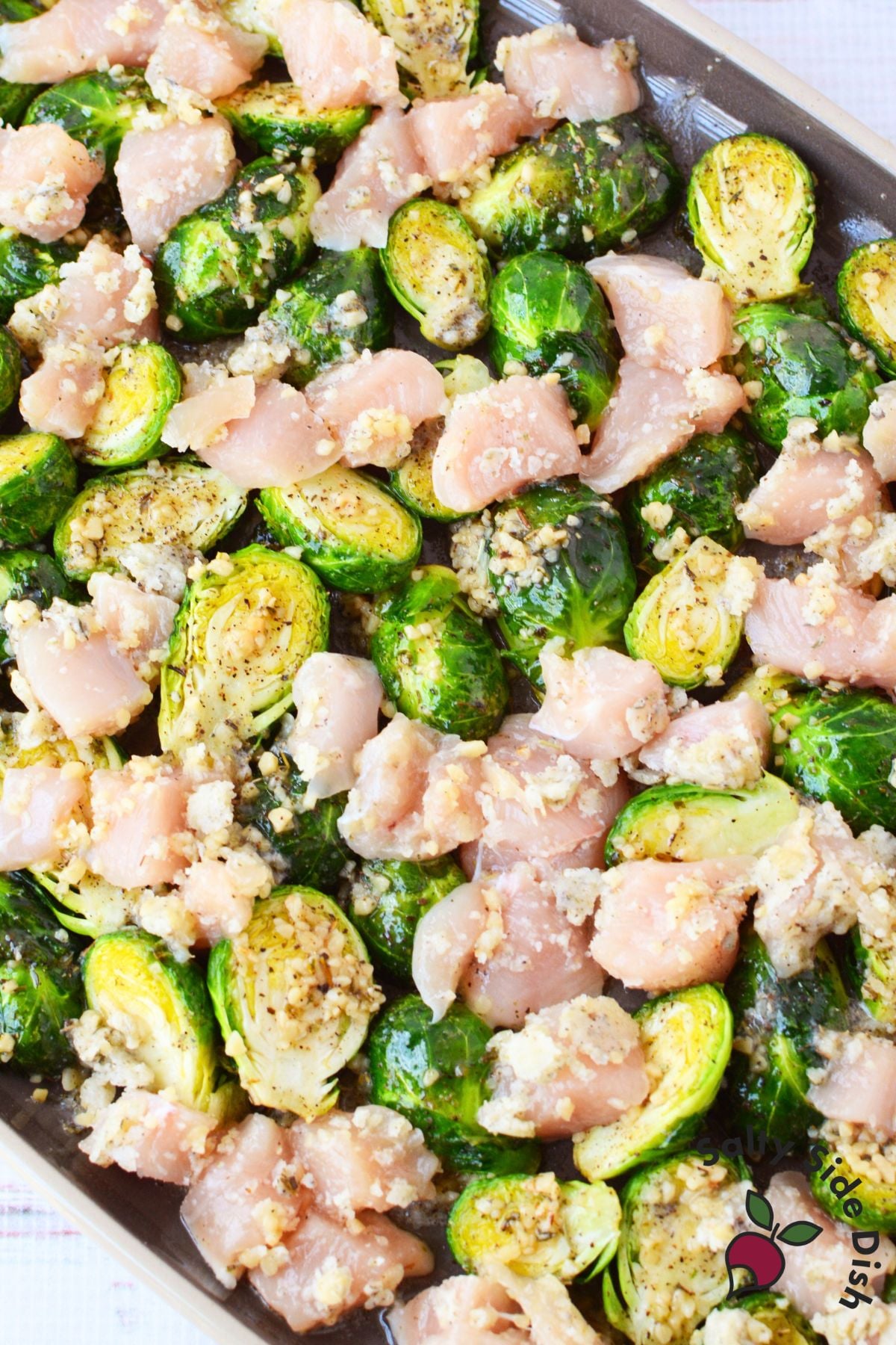 raw chicken and brussels sprouts seasoned with garlic butter spread out on a sheet pan ready to bake