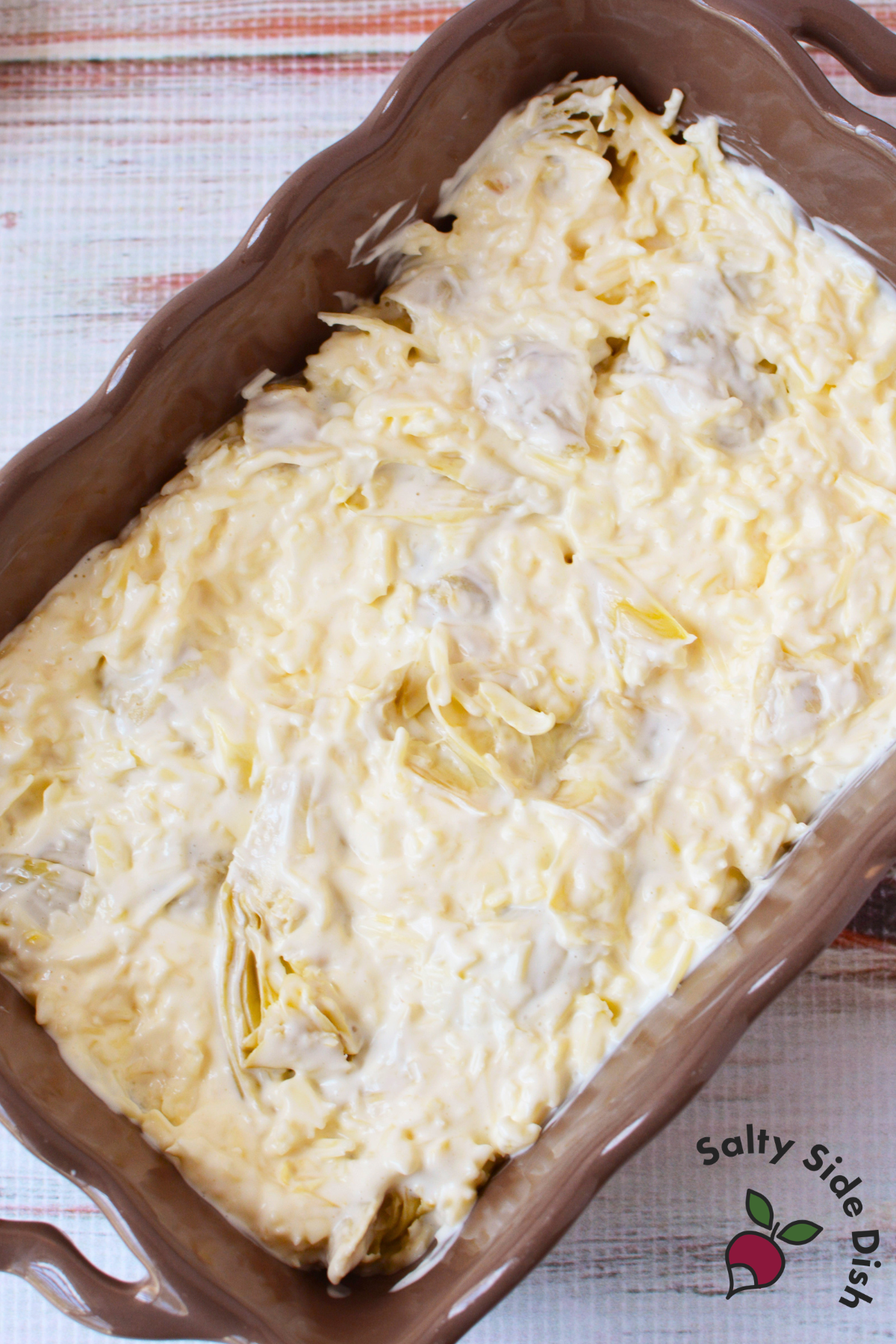 artichoke dip mixture spread evenly into a casserole dish ready to go into the oven