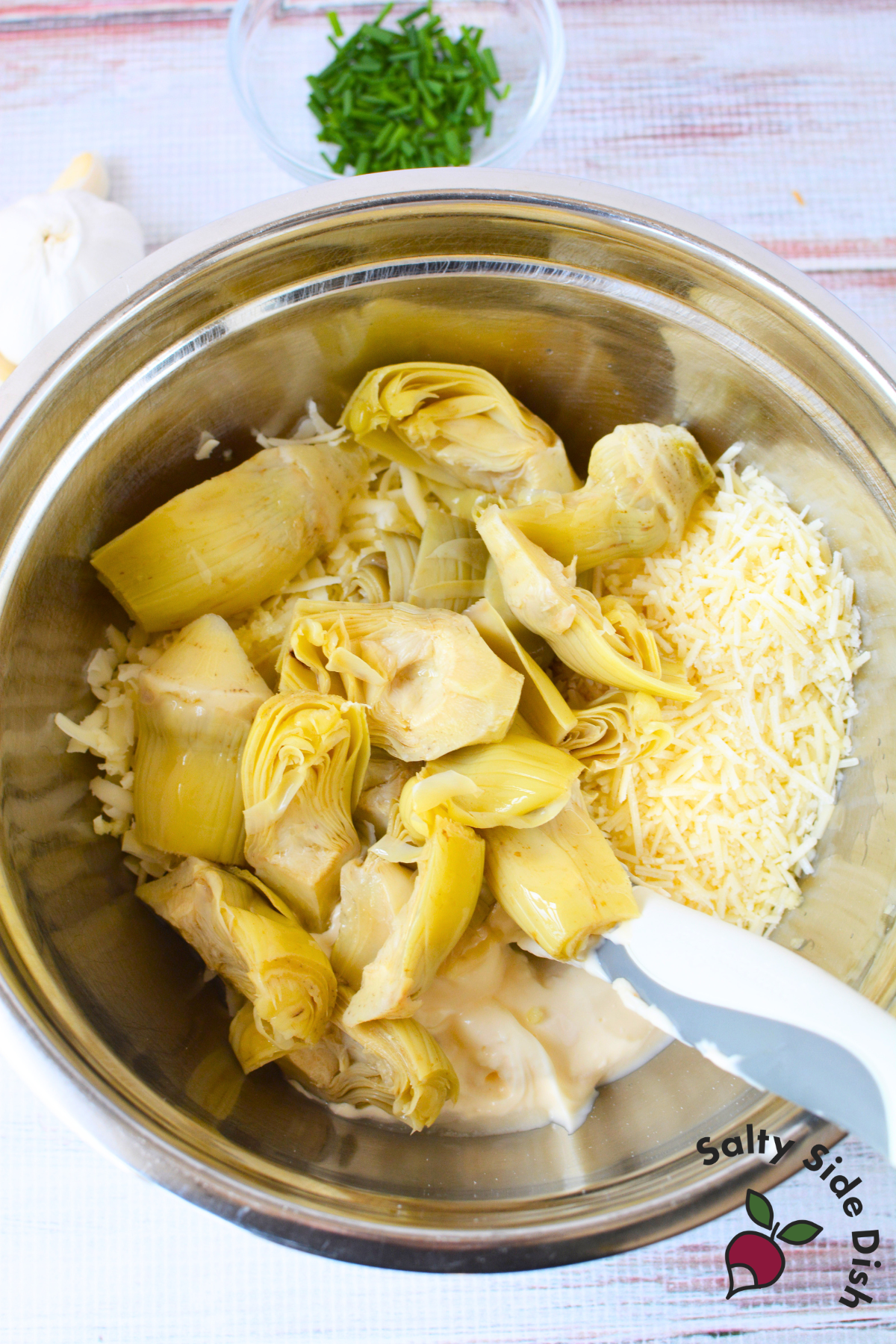 mixing bowl with quartered artichoke hearts, shredded cheese, and mayonnaise ready to be combined