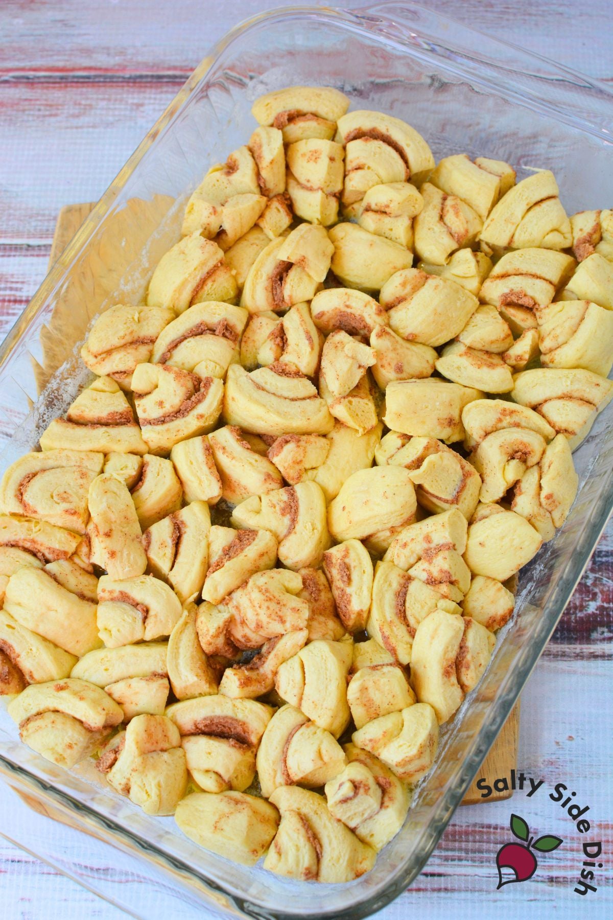 Cut up raw Pillsbury orange roll pieces arranged in a glass baking dish before baking