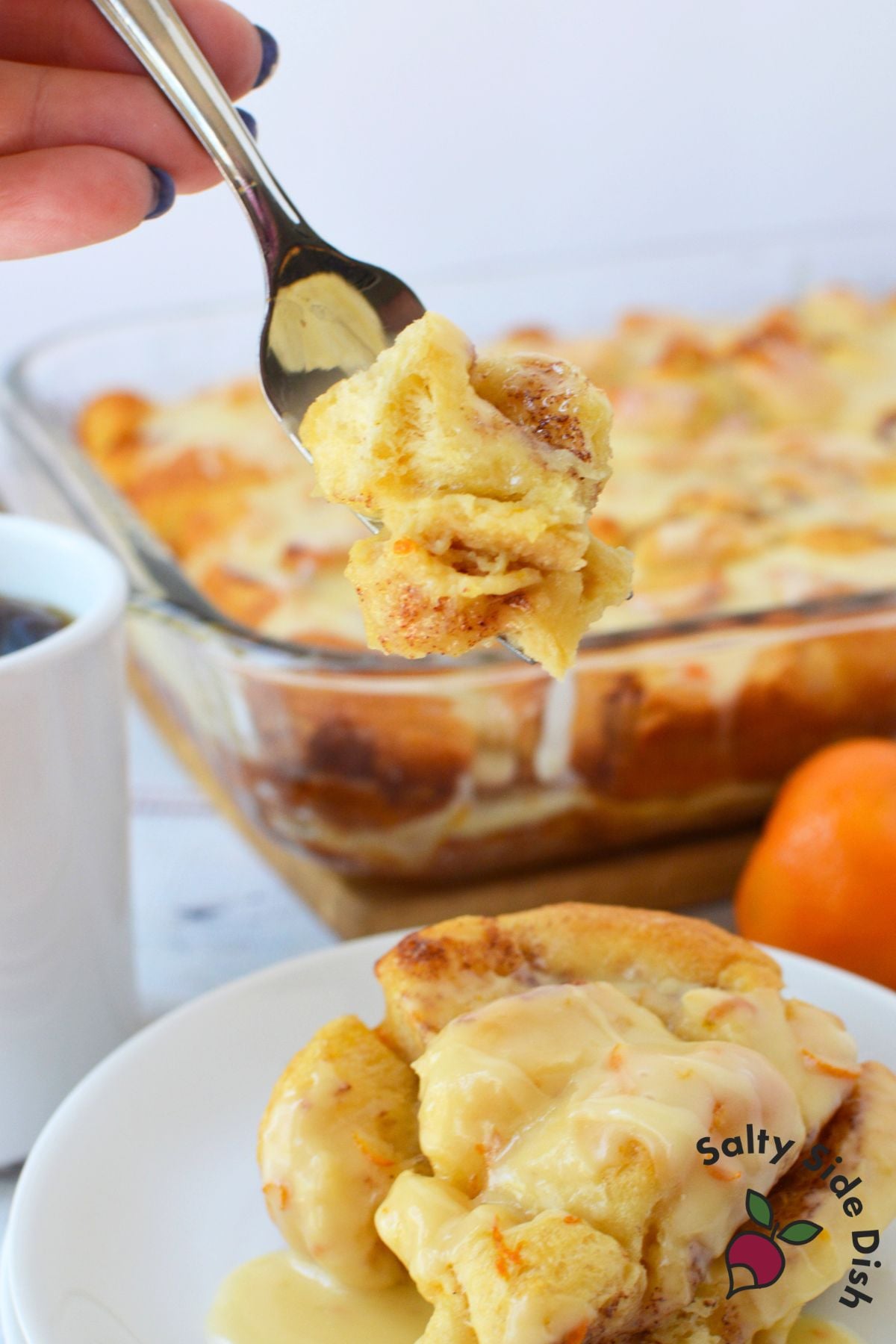 A spoon lifting a piece of orange roll breakfast casserole over a white plate topped with creamy orange glaze