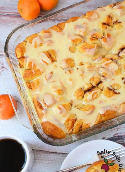 Overhead view of finished orange roll casserole covered in creamy orange glaze in a glass baking dish, surrounded by fresh oranges and a cup of coffee