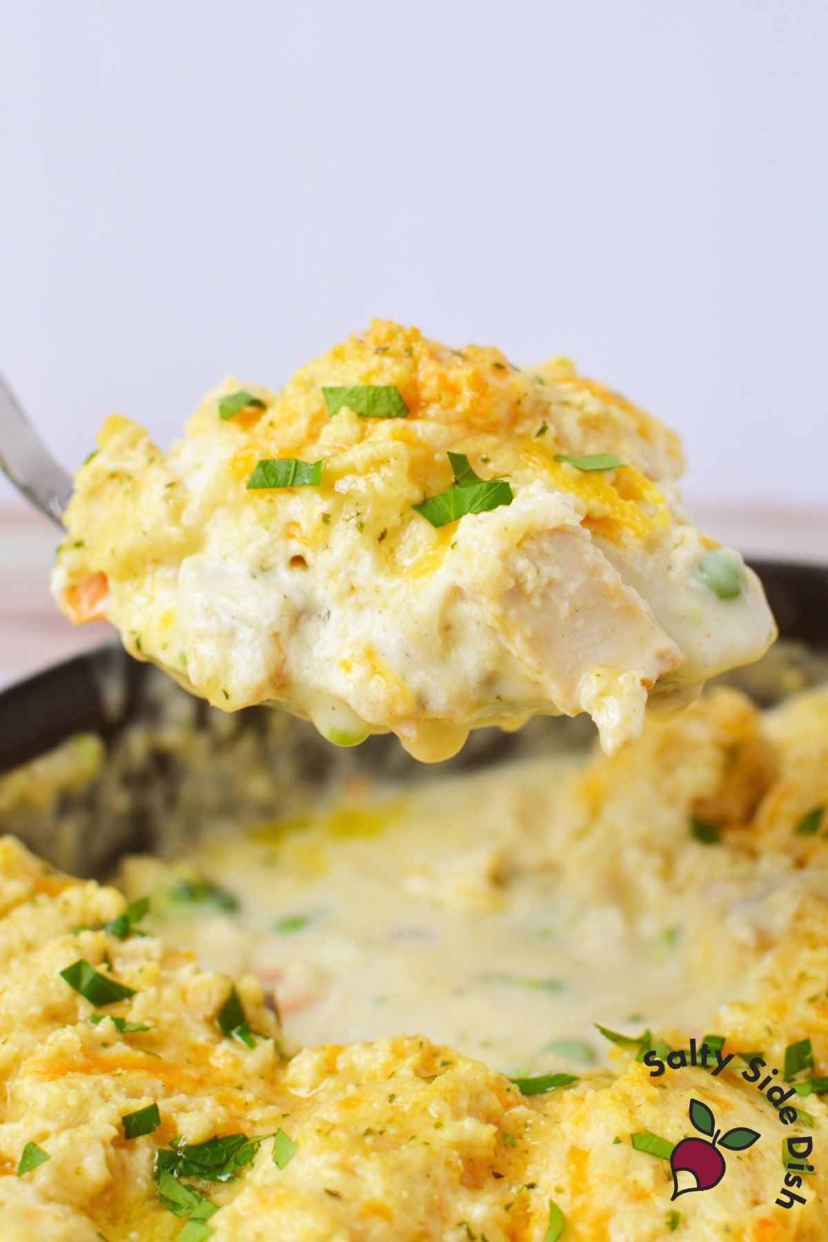 Large spoonful of creamy chicken pot pie with golden Cheddar Bay Biscuit topping lifted from a cast iron skillet