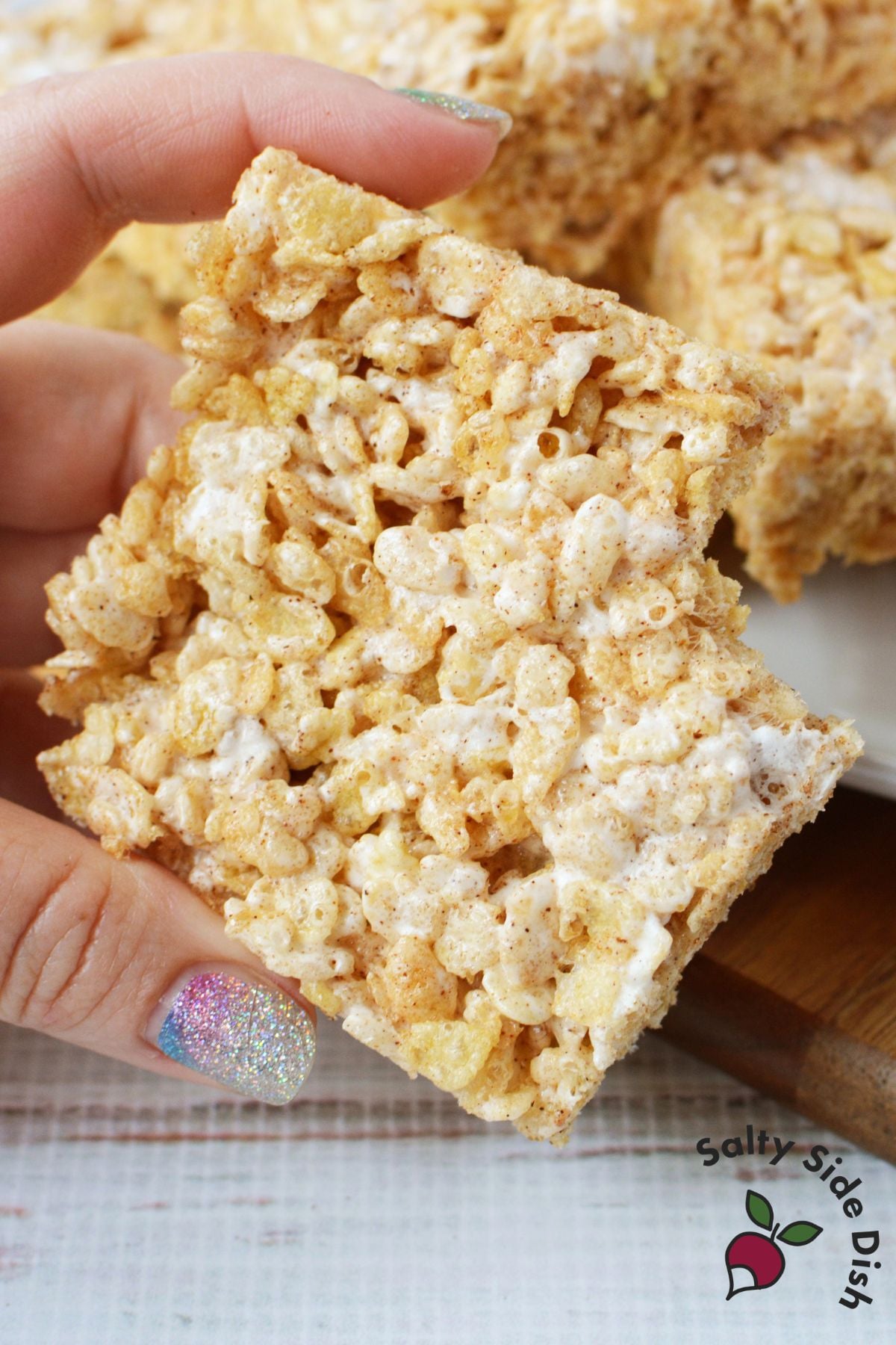 Hand holding a square of Texas Roadhouse Rice Krispie Treats showing soft, chewy texture and gooey marshmallow