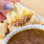 Crusty bread dipped into seasoned olive oil parmesan balsamic bread dip close up